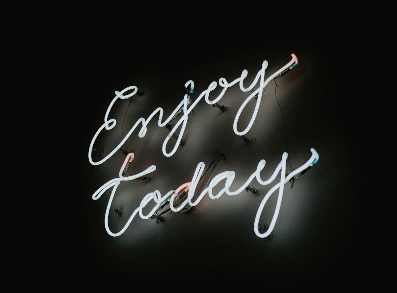 Neon sign with motivational message 'Enjoy Today' on a dark background.