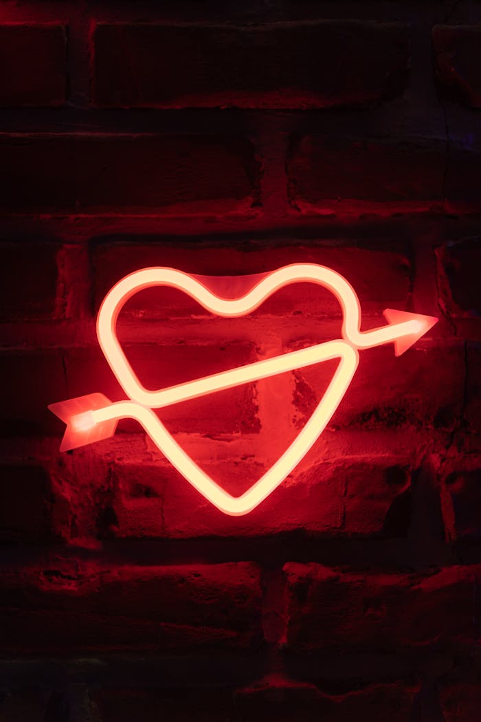 Bright neon heart with arrow sign on a rustic brick wall, creating a romantic and bold ambiance.
